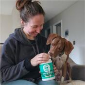 Woman smiling and giving her dog daily joint care treat while sitting on couch