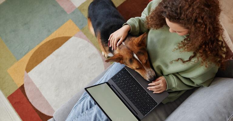 woman using laptop and petting dog while dog sit head in her lap